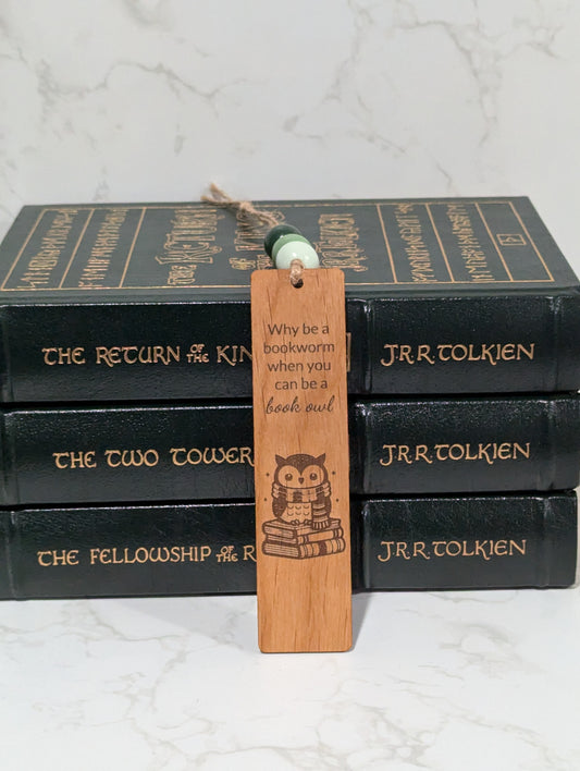 Wooden bookmark with the design of an owl wearing a scarf perched on a bookstack. Text above the design reads Why be a worm when you can be a book owl.