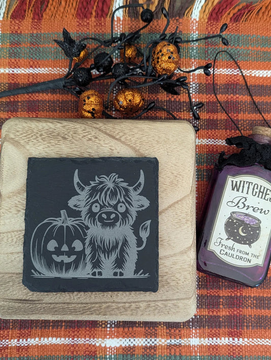 Slate coaster engraved with a highland cow and a pumpkin with Halloween decor.