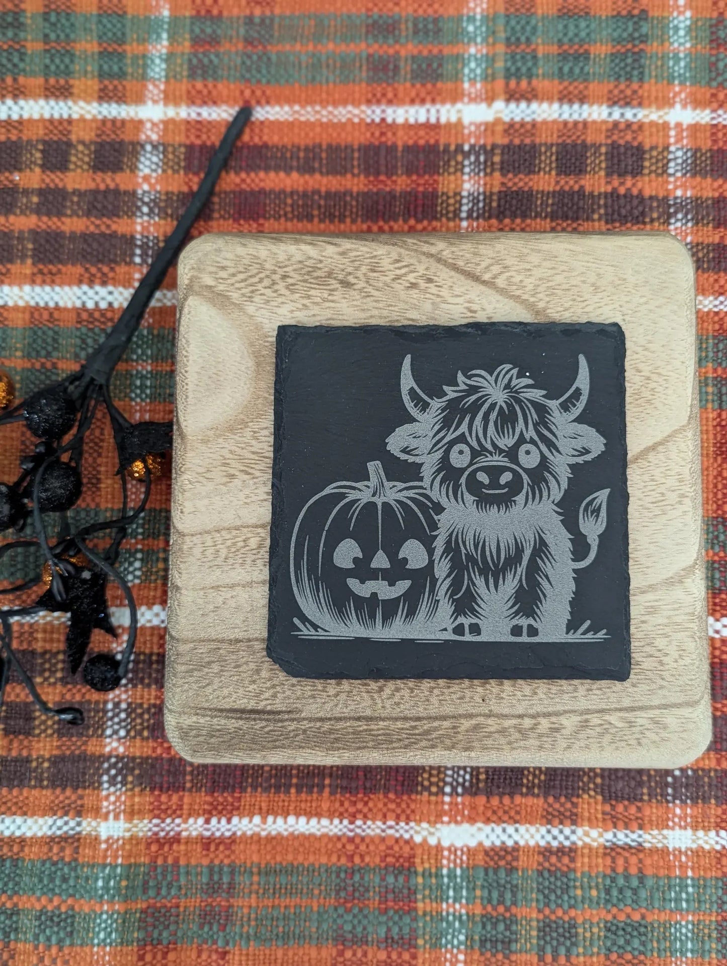 Slate coaster engraved with a highland cow and a pumpkin with Halloween decor.