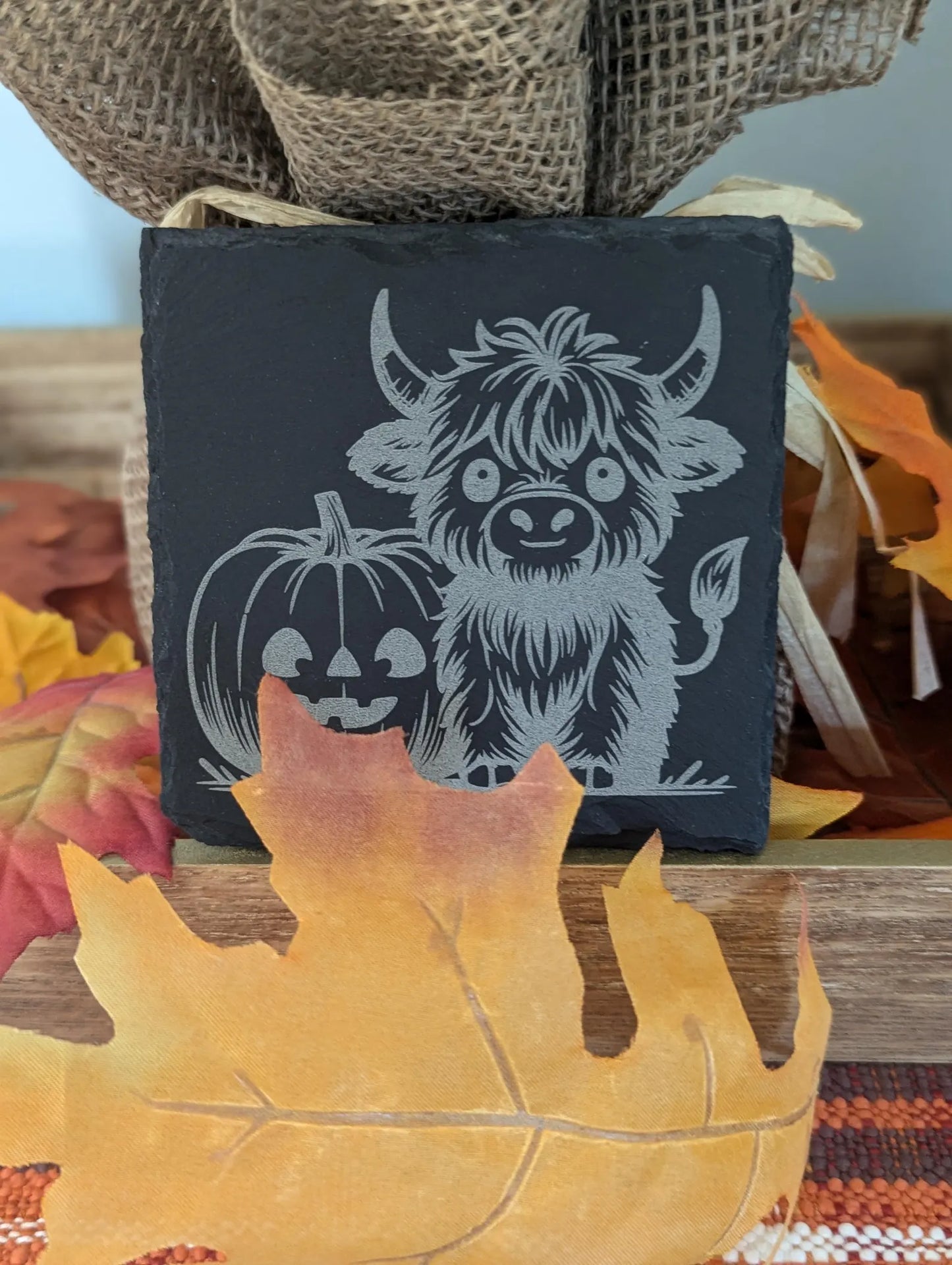 Slate coaster engraved with a highland cow and a pumpkin with fall decor.
