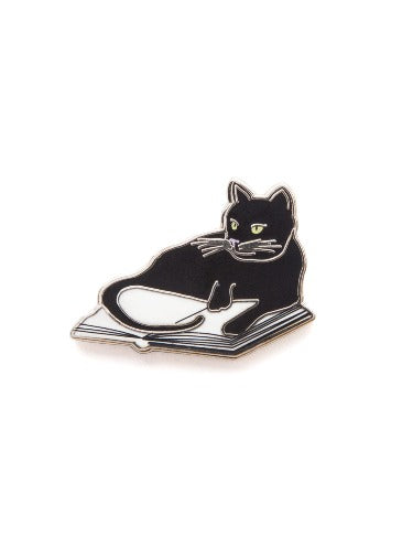A pin in the design of a black cat laying on an open book.