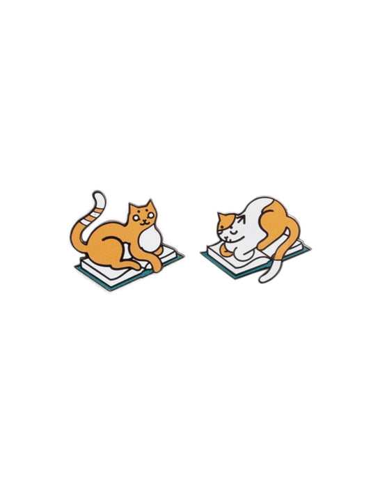 Two pins of orange-and-white cats laying on books.