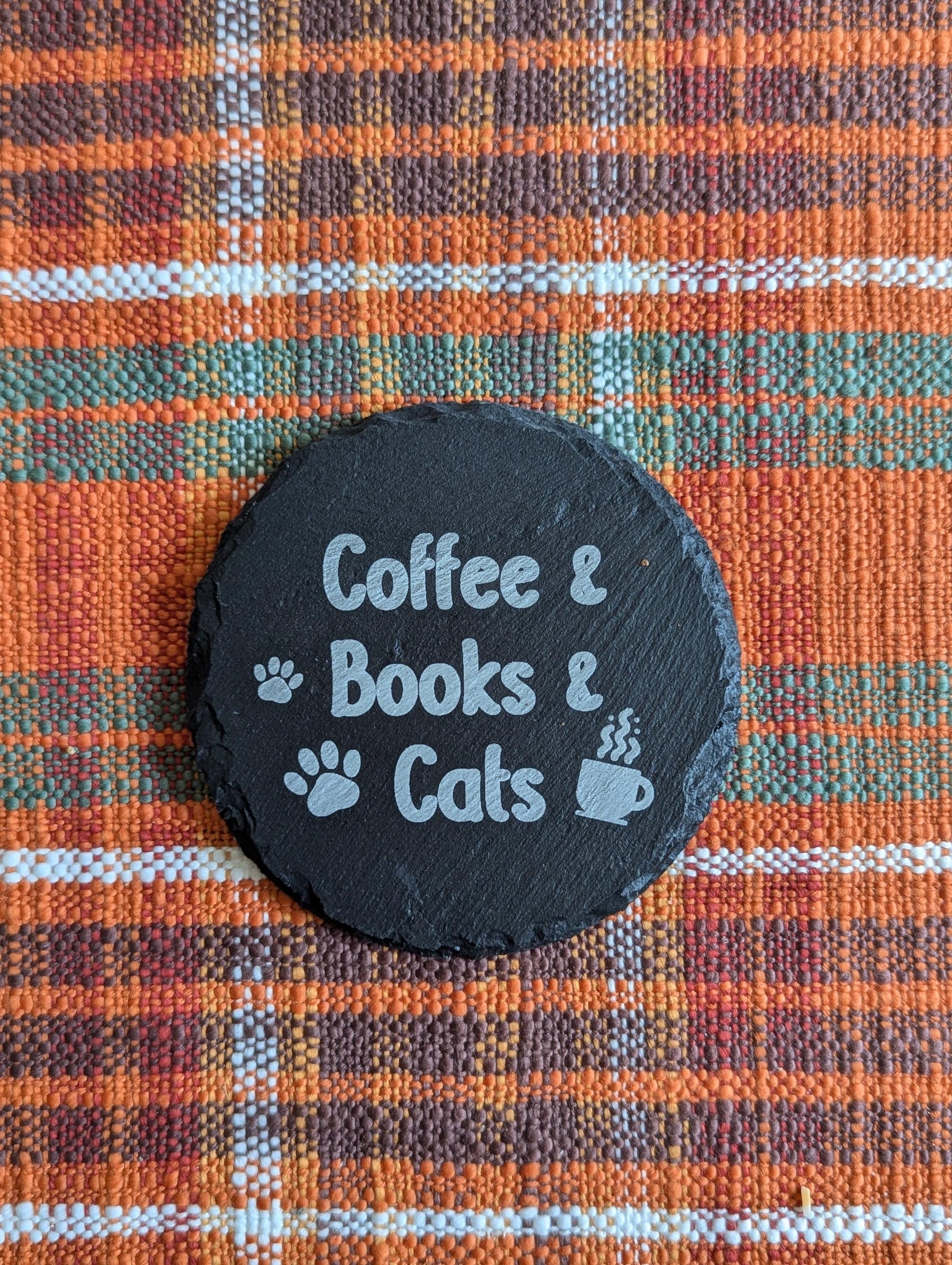 Slate coaster laser-engraved with text that says Coffee & Books & Cats; with some paw prints and a steaming coffee cup.