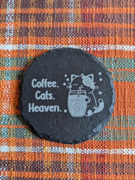 Slate coaster with a laser-engraved design of a cute cat sipping coffee alongside text that says coffee, cats, heaven.