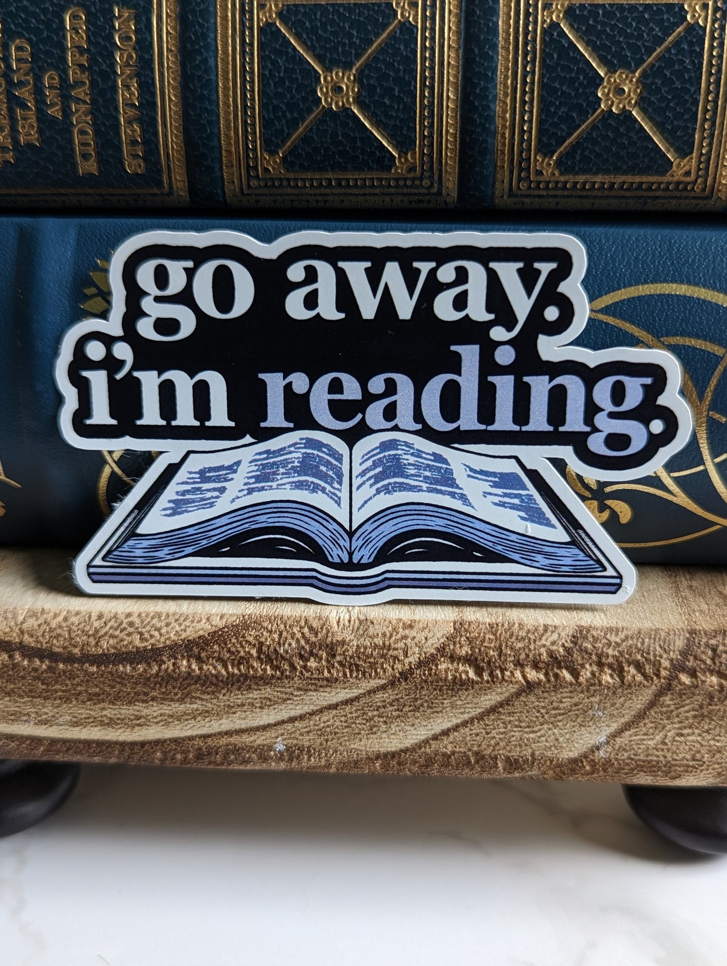 AA sticker with text on top that says "Go away. I'm reading" above an open book.