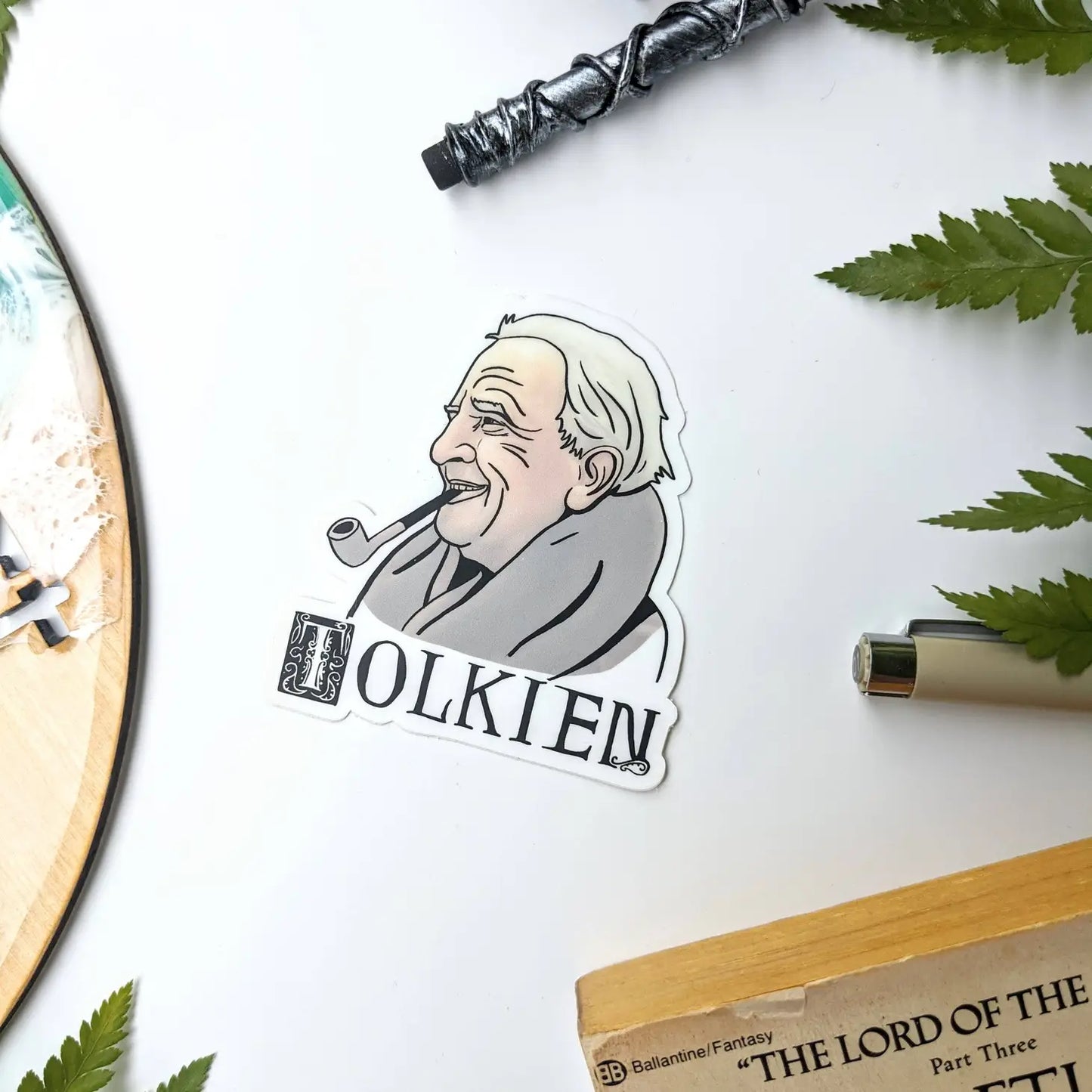 A sticker depicting J.R.R. Tolkien. The stick shows a smiling old man smoking a pipe. Vintage text  beneath the man says "Tolkien".