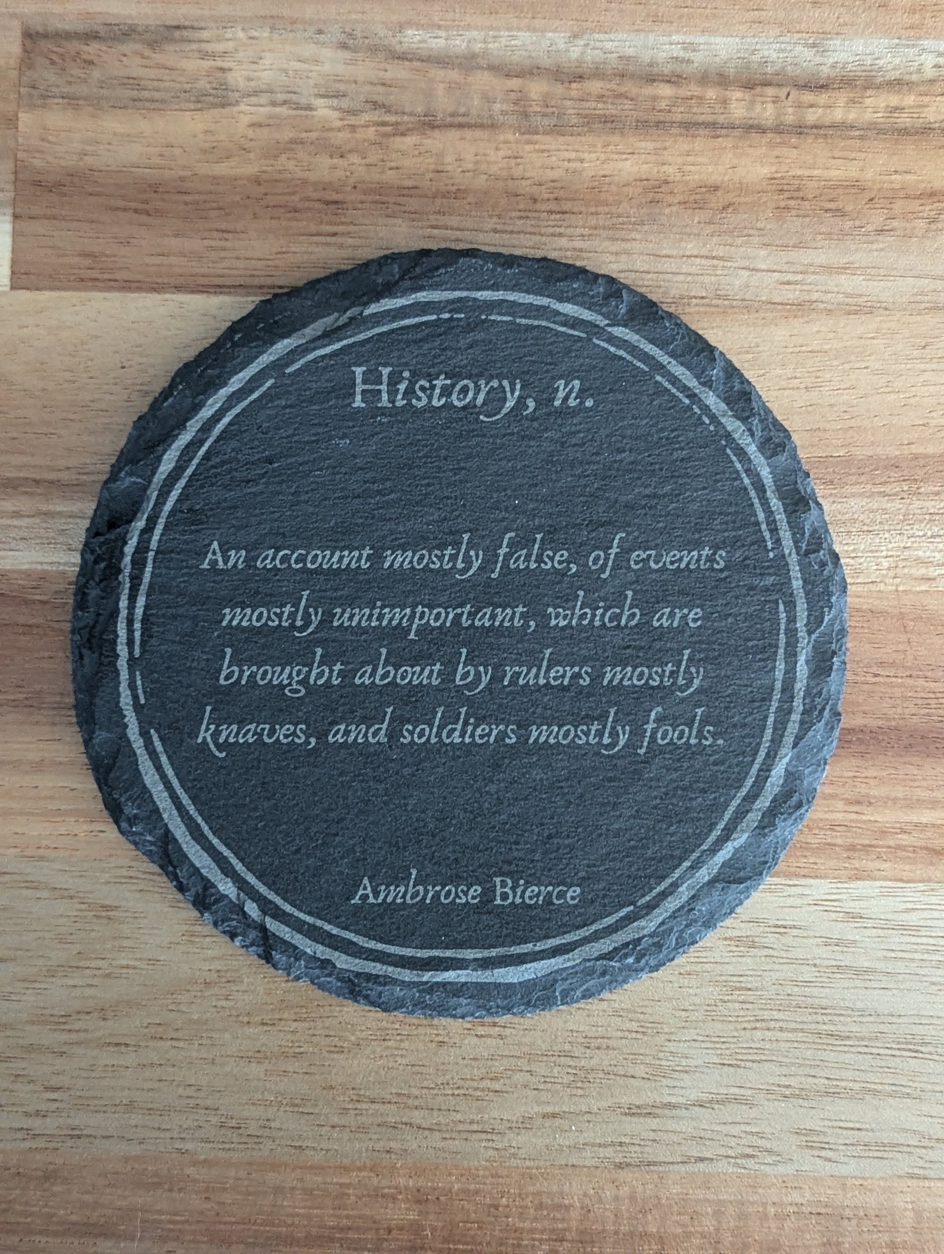 Slate coaster with a laser-engraved design of a definition of history by Ambrose Bierce.