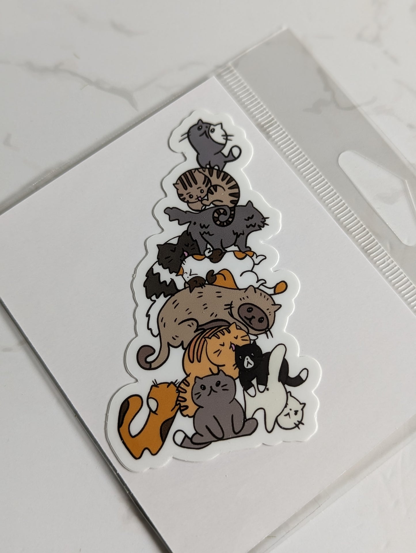 A sticker in the design of a stack of variously-colored cats.
